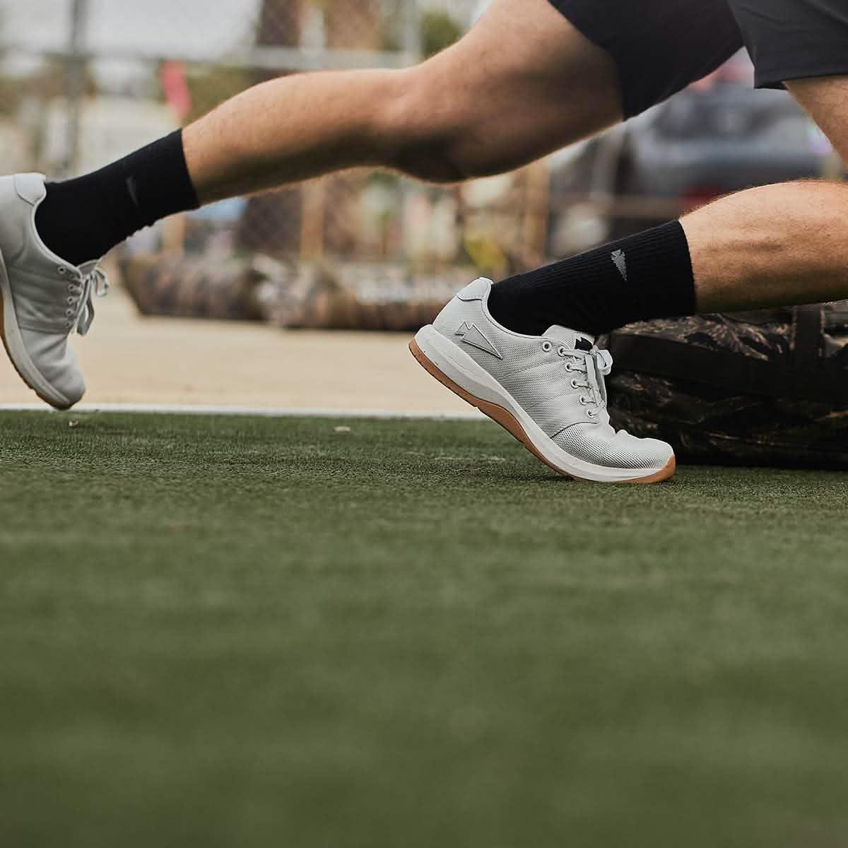 Person wearing white sneakers and black socks running on artificial turf in outdoor training setting