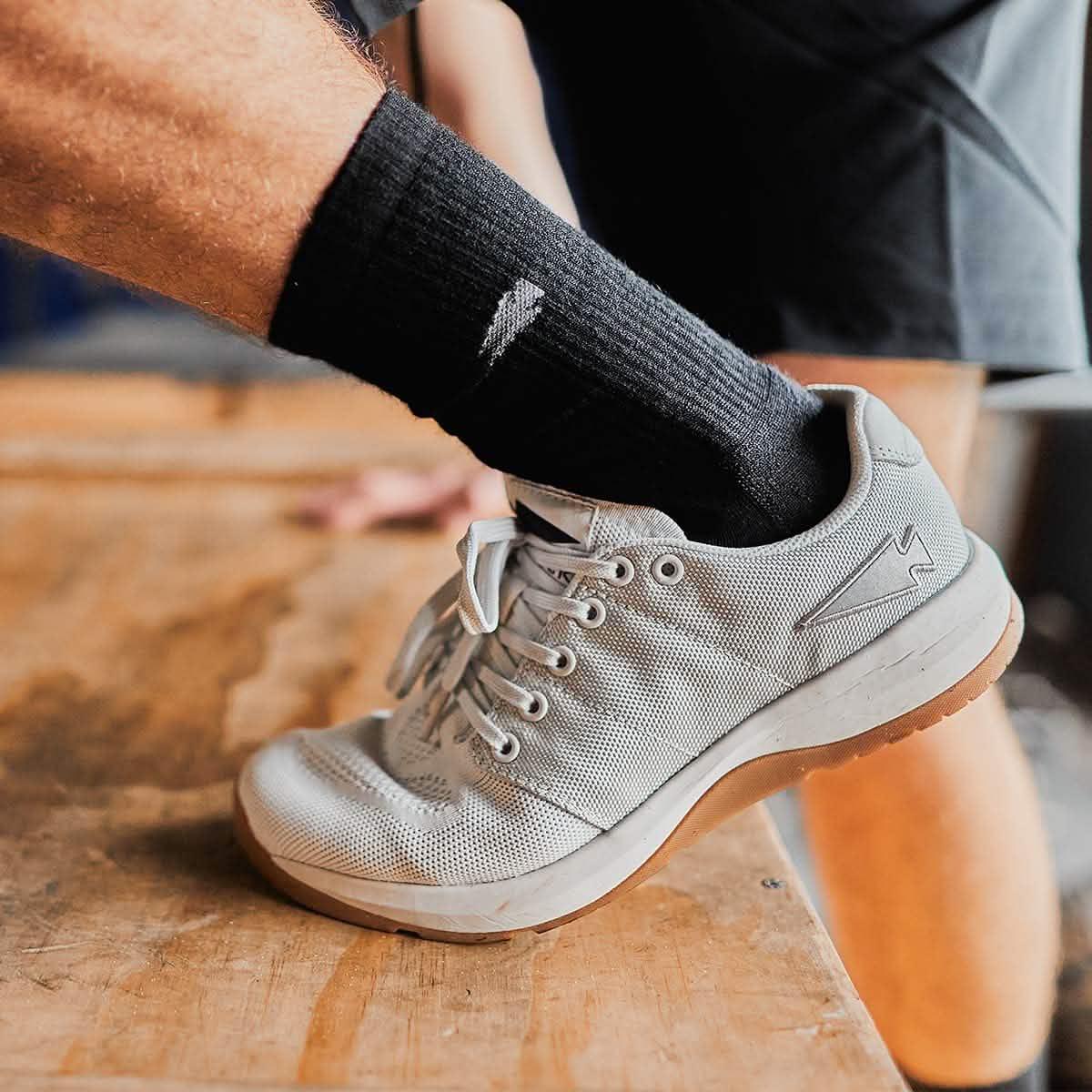 Close-up of a person's foot wearing gray GORUCK Lunar Rock training shoe and black socks on wooden platform