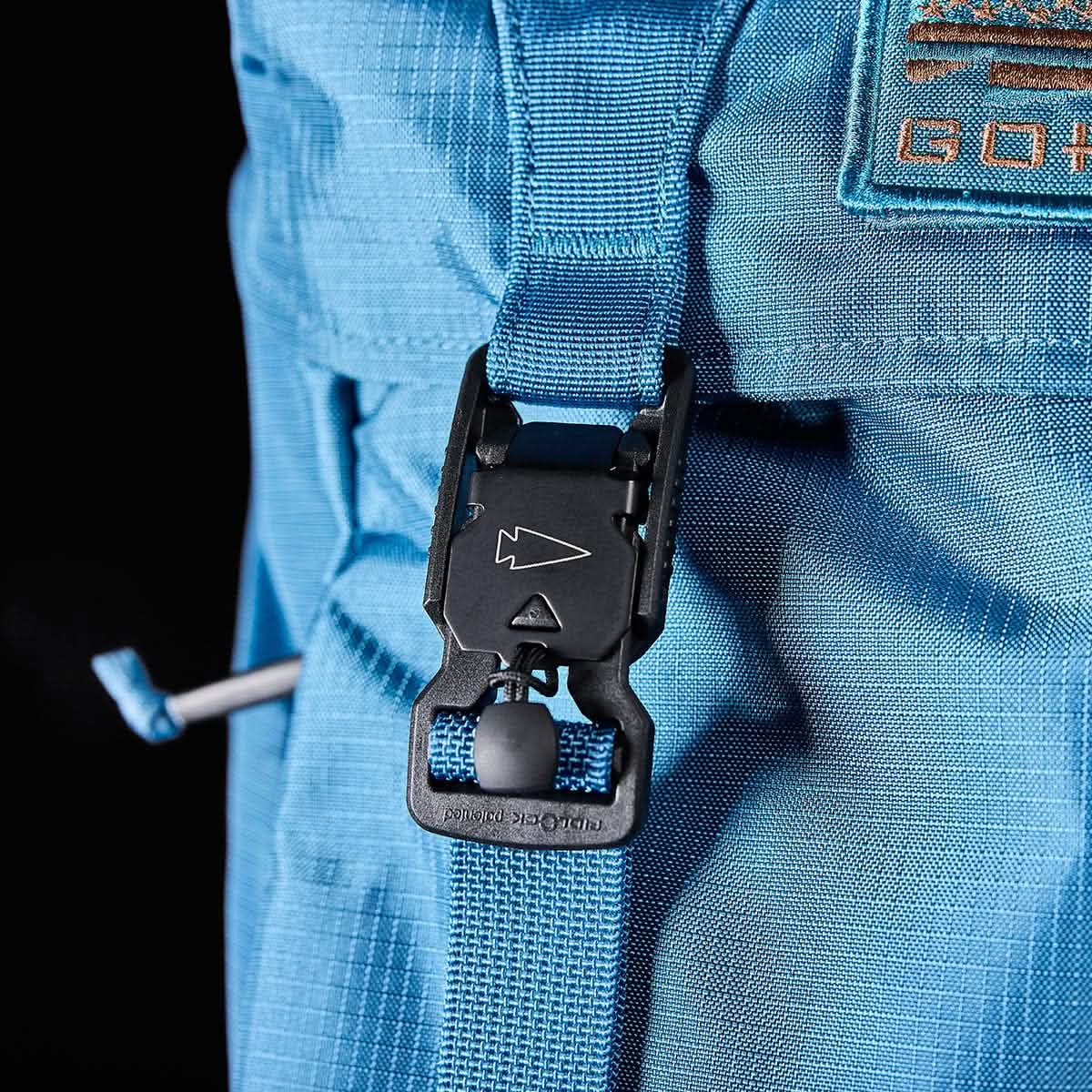 Close-up of the GORUCK M23 rucksack in Tidal Blue with Speed Tan accents, featuring a black buckle fastener and a short strap. The textured fabric resembles that of an M1945 field pack, with part of the orange logo visible on the upper right corner of the 21L backpack.