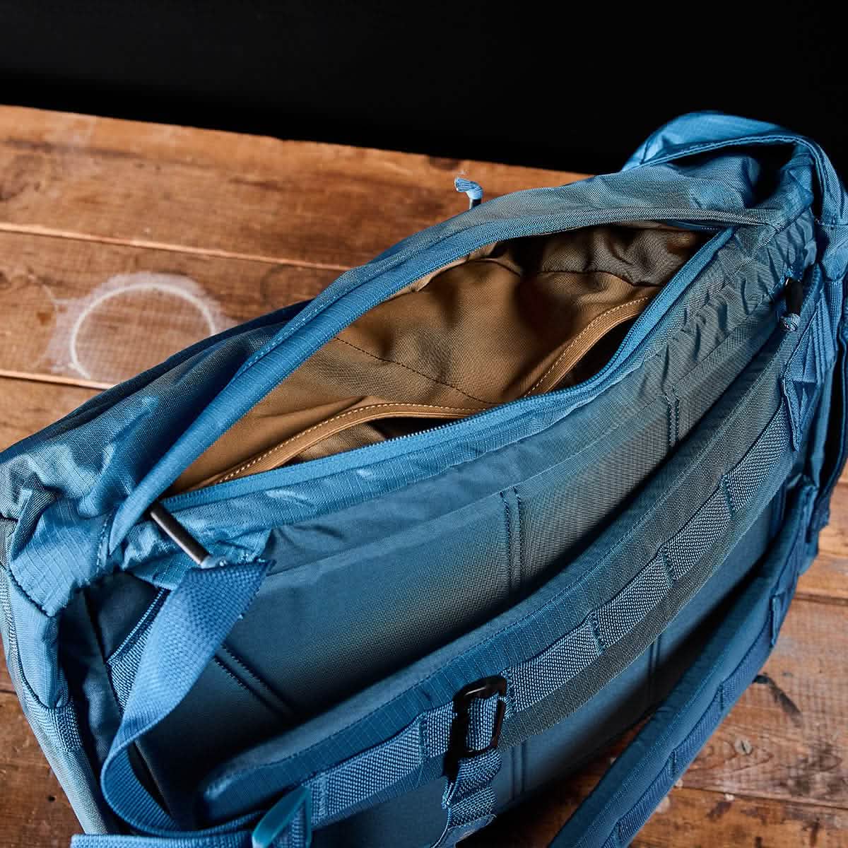 The M23 - Ripstop ROBIC® rucksack by GORUCK in Tidal Blue + Speed Tan is open, showcasing its tan interior lining. It rests on a rustic wooden surface against a dark background, capturing the rugged charm reminiscent of an M1945 field pack.