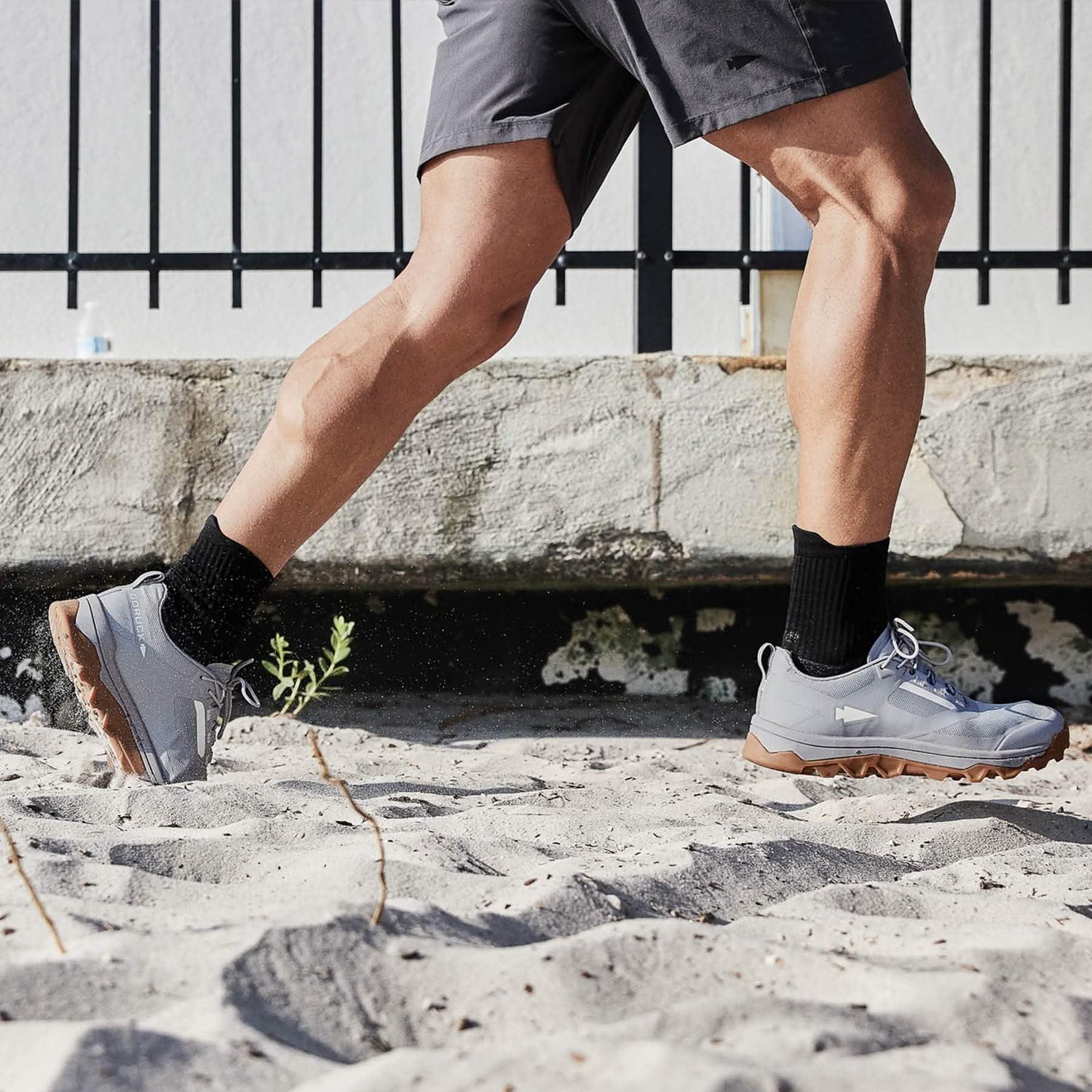 Man rucking on sand wearing GORUCK grey trail shoes and black socks, outdoor fitness apparel