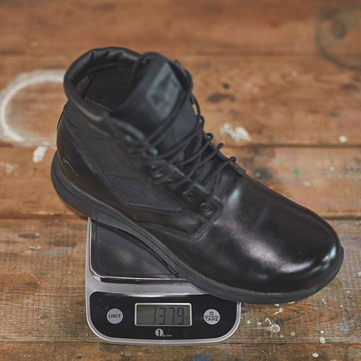 A black boot rests on a digital scale displaying a weight of 1.379 kilograms on a wooden surface.