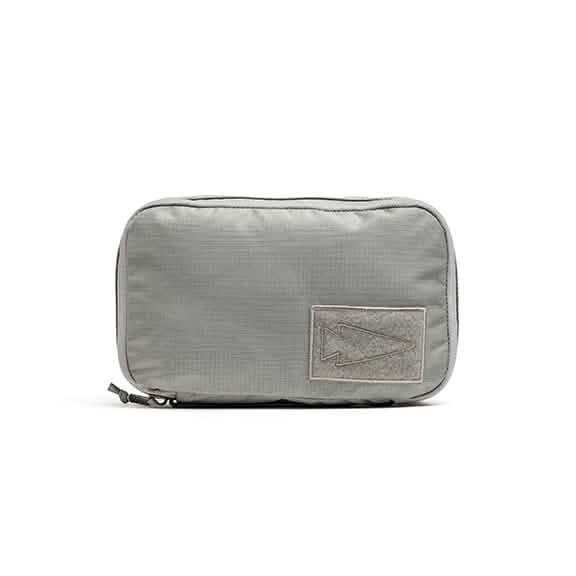 Introducing the GORUCK Shadow Pockets - Ripstop ROBIC®, a rectangular travel pouch in light gray. Crafted from durable 420D ROBIC Nylon, it features a zipper closure and a stitched arrow design on a textured patch at the front. This robust material enhances rucksack organization and is ideal for conveniently carrying small items.