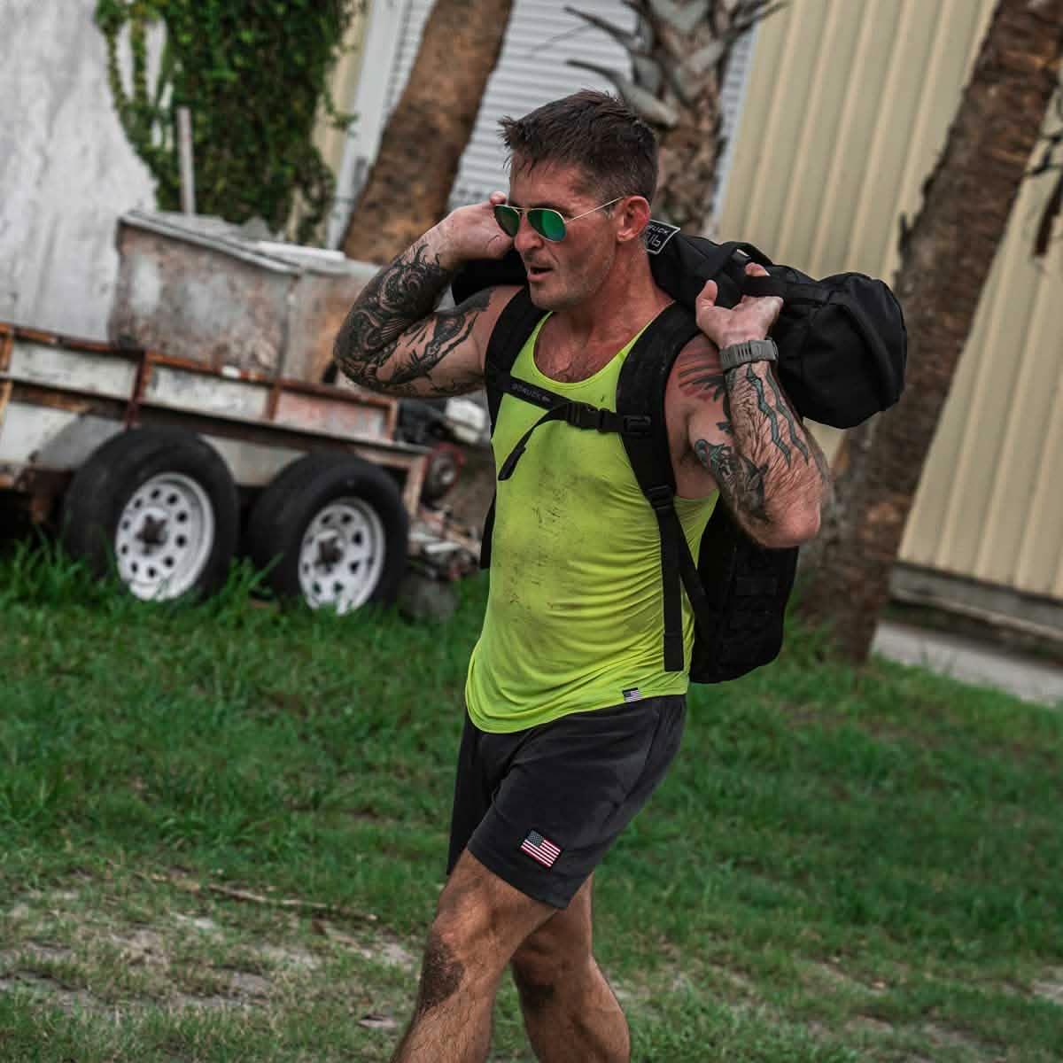 Athletic man wearing acid lime GORUCK men's performance tank and black shorts carrying a weighted rucksack outdoors