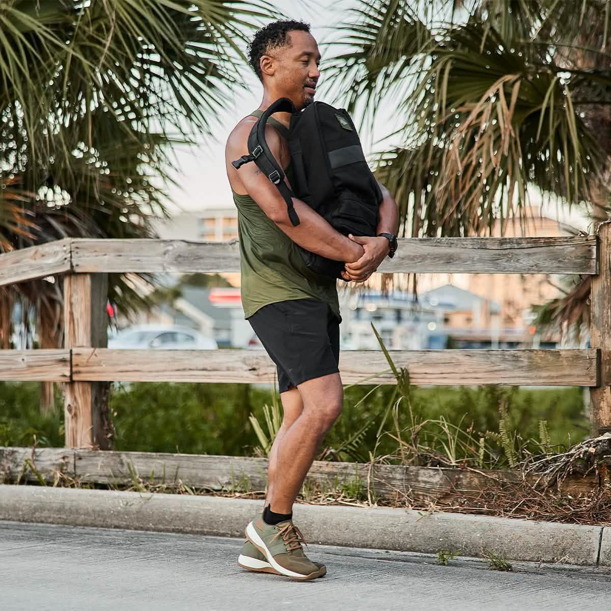 Man rucking outdoors wearing GORUCK gear, olive tank top, black shorts, training shoes