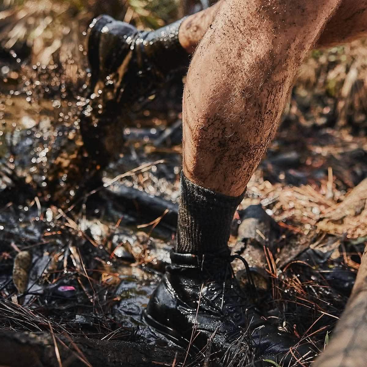 Close-up of muddy legs and black rucking boots splashing through a wet forest trail