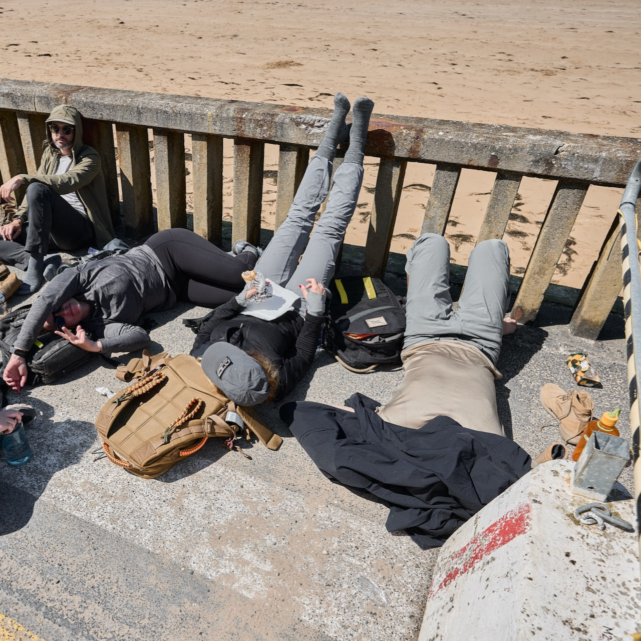 Three people relax on their backs by a sandy beach, legs up on a railing, enjoying the sun and showing off their Merino Challenge Socks - Crew.