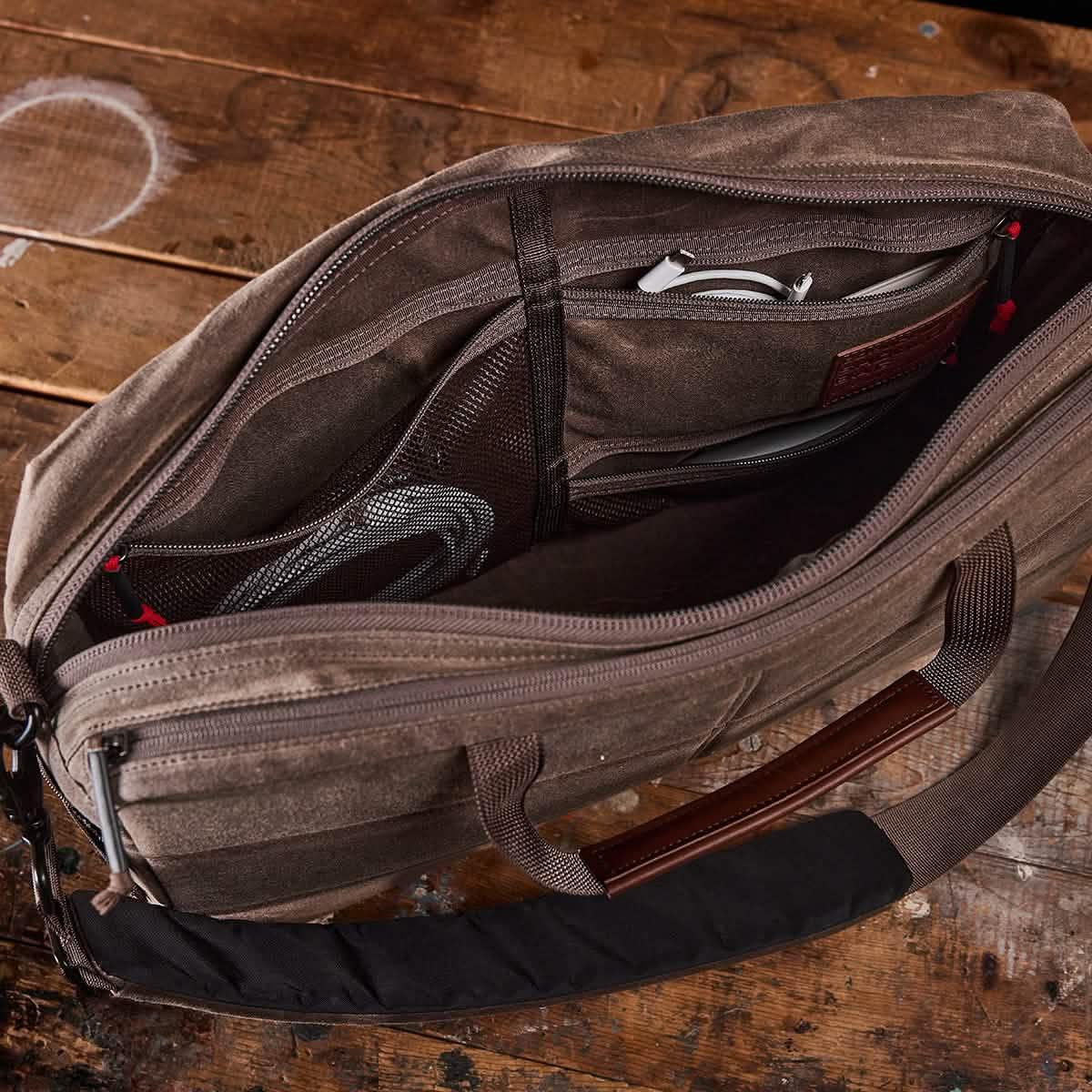 Open brown GORUCK laptop bag on wooden surface showing organized interior pockets with cables and accessories