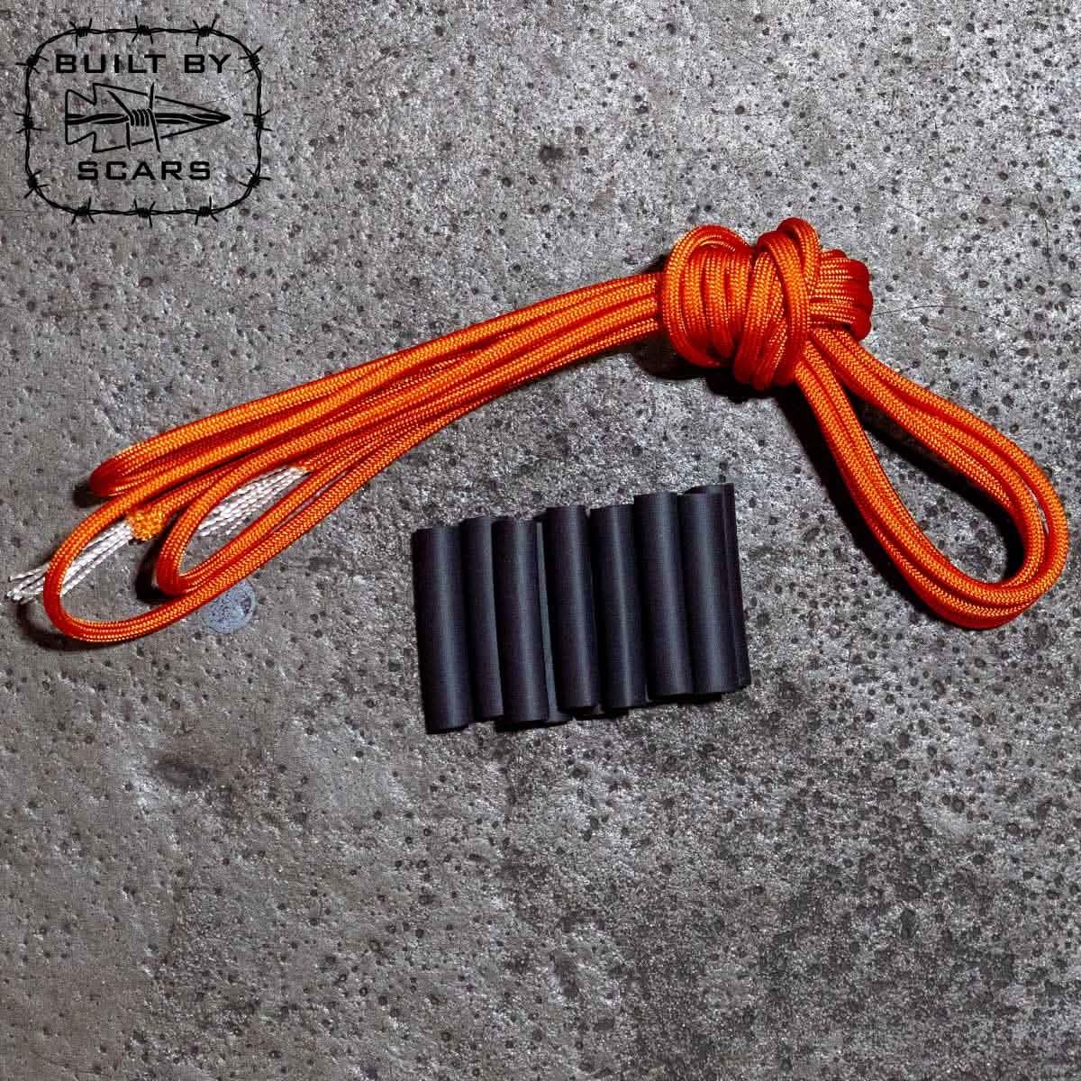 Orange paracord with six black heat shrink tubes on textured concrete surface, GORUCK gear detail