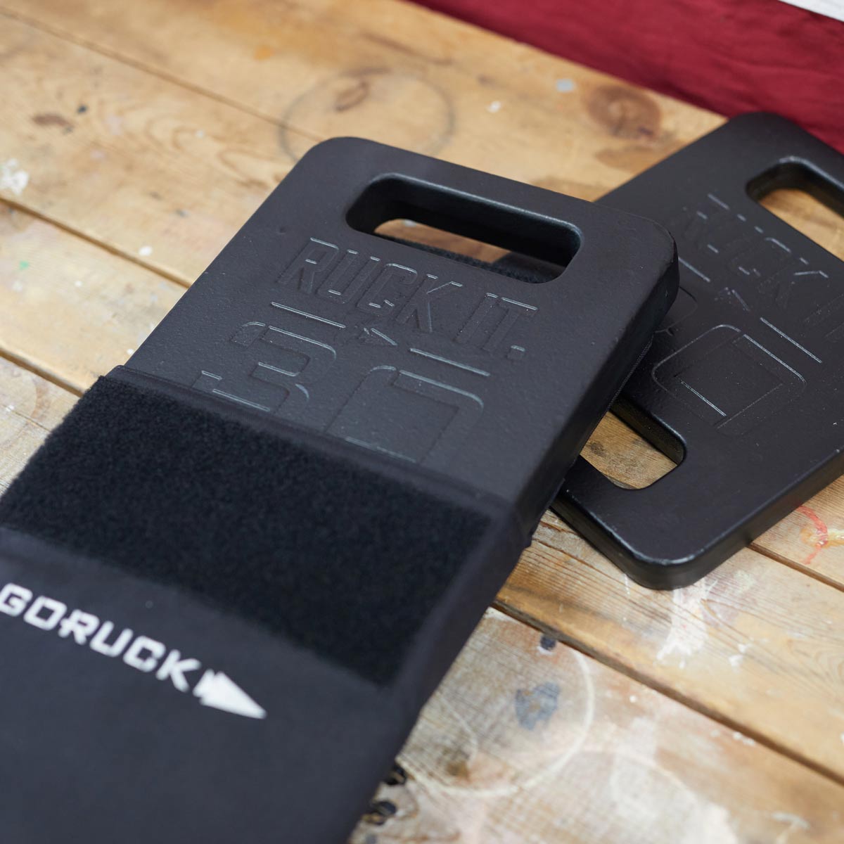 Two black GORUCK ruck plates with handles sit on a wooden surface.