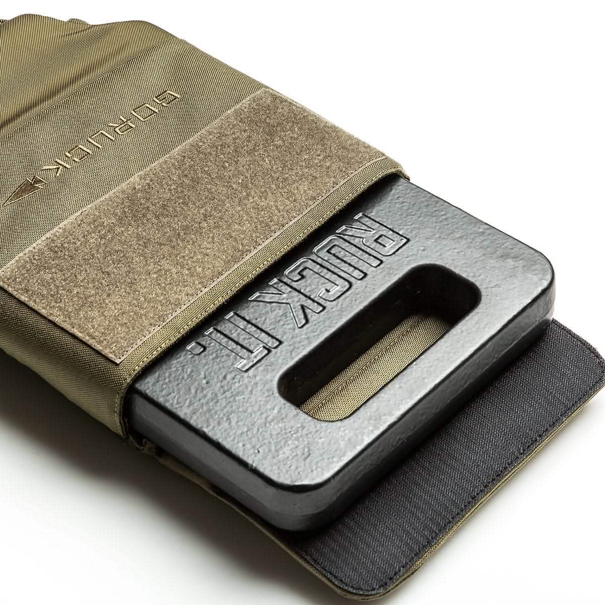 A weighted ruck plate is partially inserted into the tan, robust Ruck Plate Carrier 3.0 from GORUCK, secured with a Velcro flap. Crafted from 1000D CORDURA, this durable carrier is ideal for fitness or military training and offers ergonomic lumbar support. The black plate features an embossed rectangular hole with the text RUCK PL.