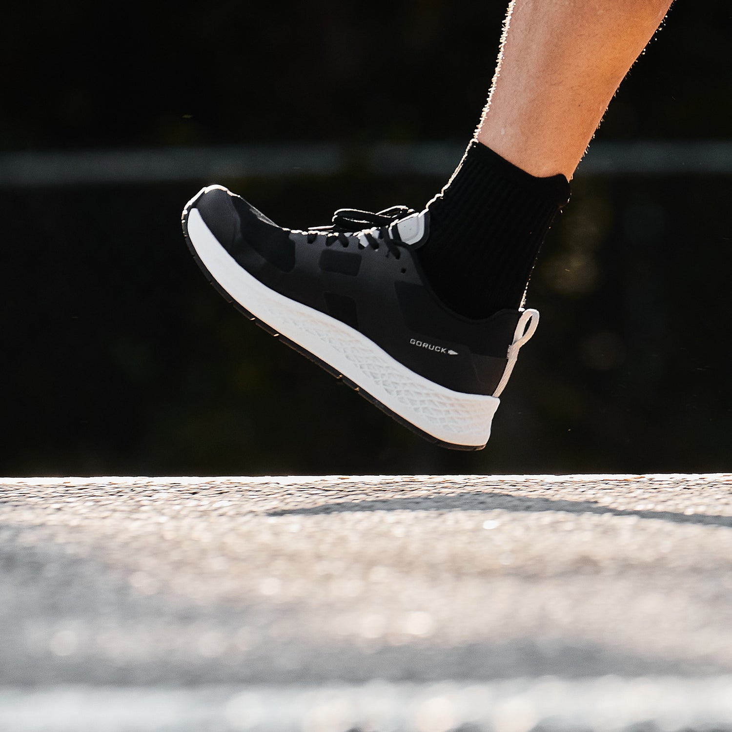 A person wearing black sneakers and black socks jogging outdoors, close-up on the foot mid-step.