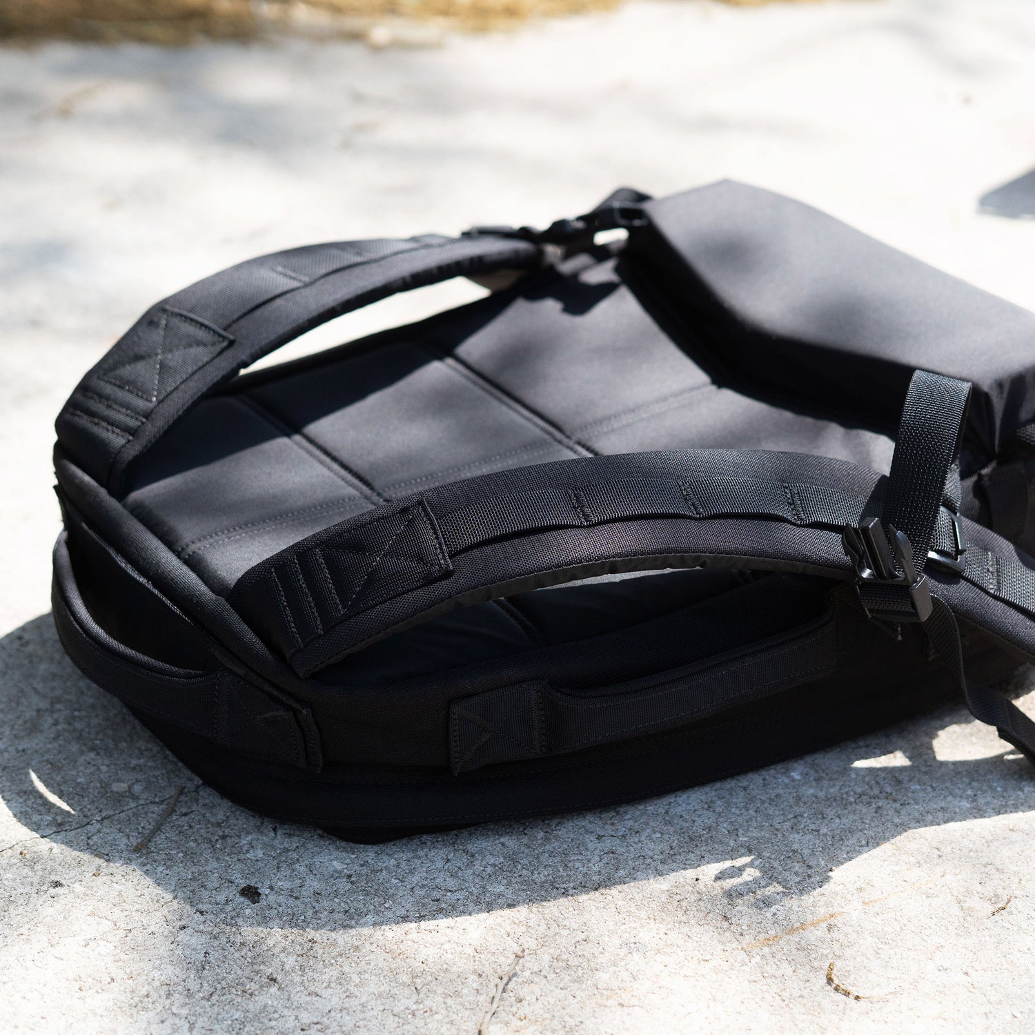 The Rucker 5.0 rests on a sunlit concrete surface, showcasing its straps and padded back panel with lumbar support.