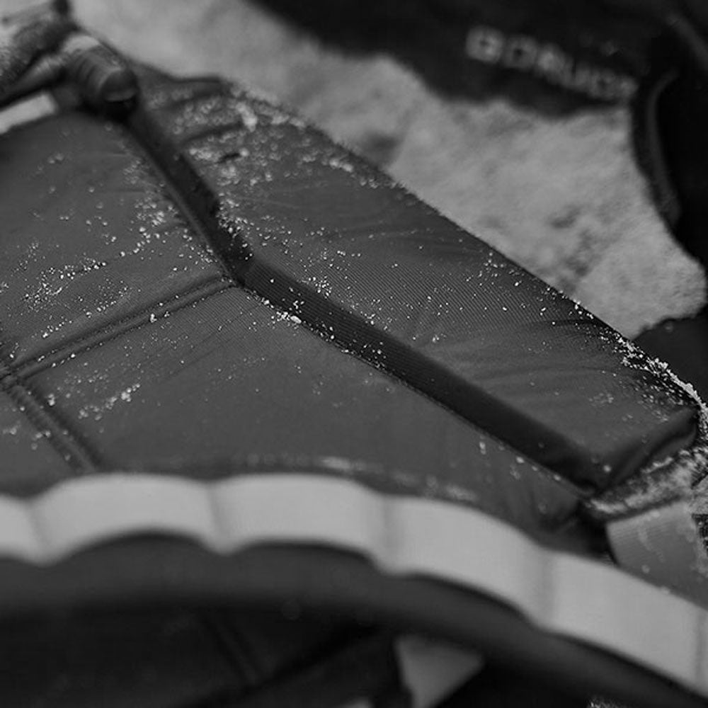 Close-up of a black backpack with sand scattered on it, shown in black and white.