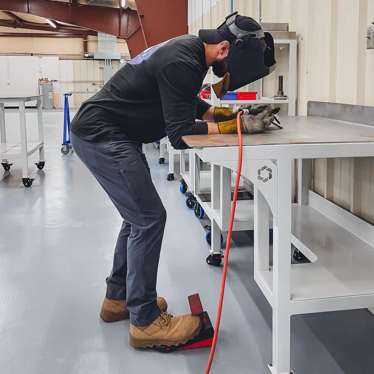 Man welding at workbench wearing GORUCK safety boots and protective gear in workshop