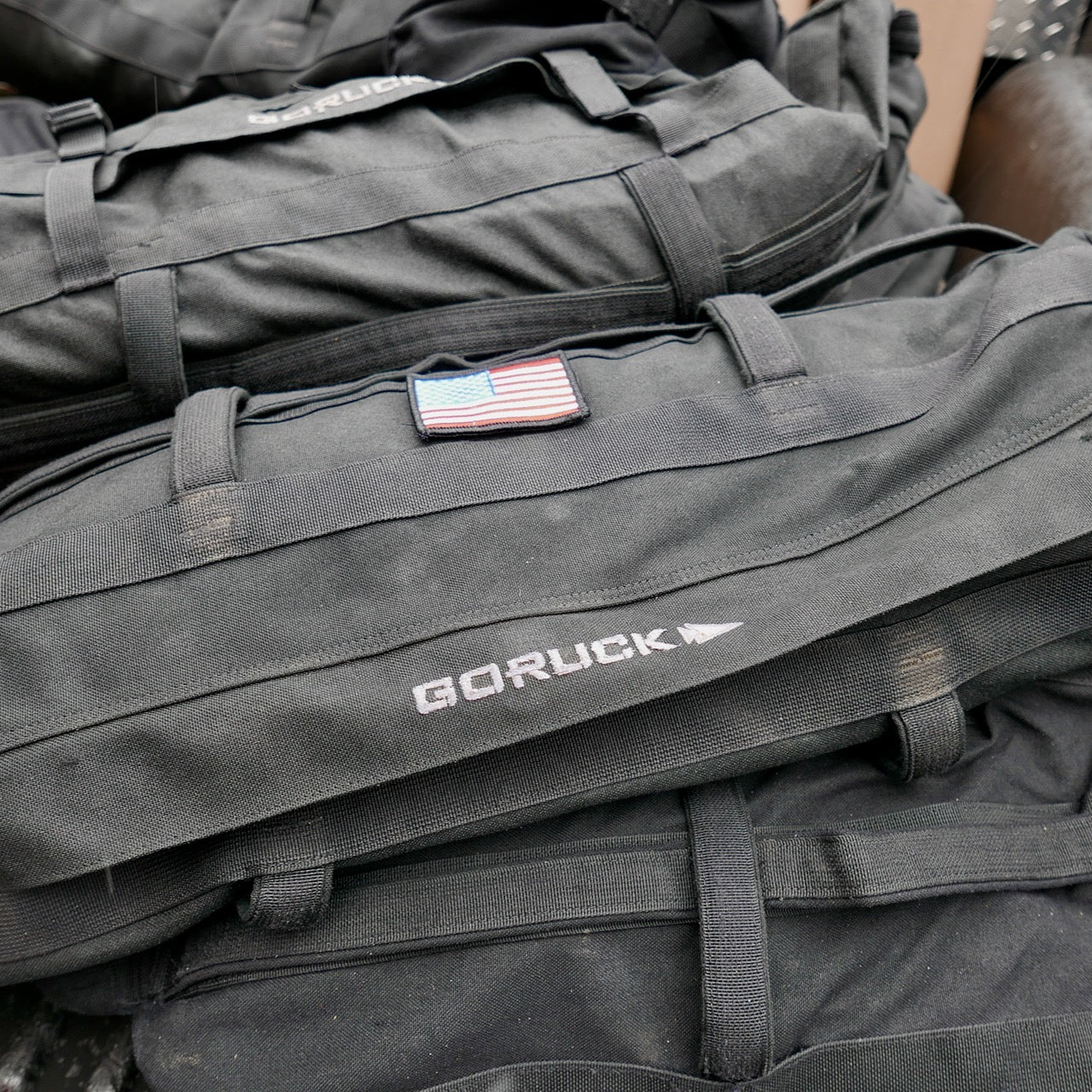 A black GORUCK Sandbag Kit (w/ Filler Bag) with an American flag patch lies among other heavy-duty sandbags, all built tough for training and backed by a Lifetime Guarantee.