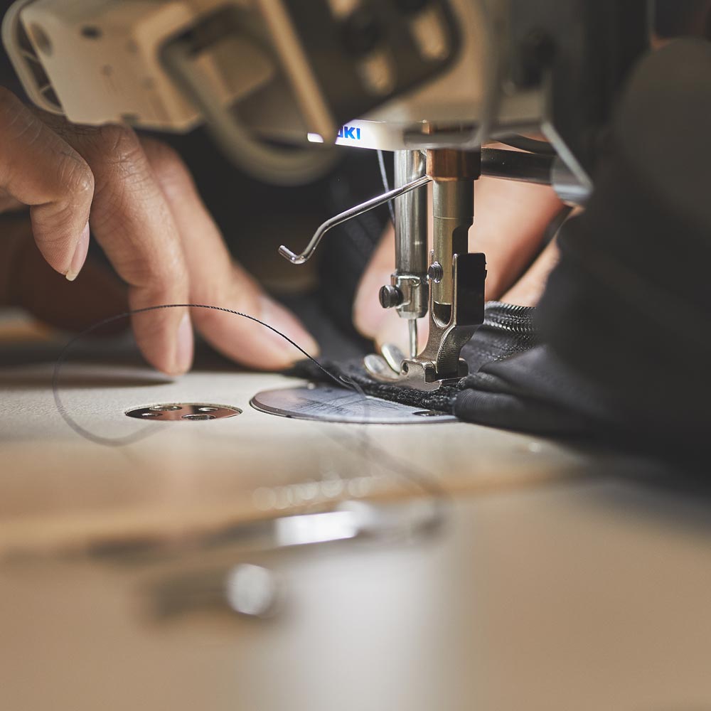 Close-up of hands sewing black fabric with a sewing machine, needle and thread visible.