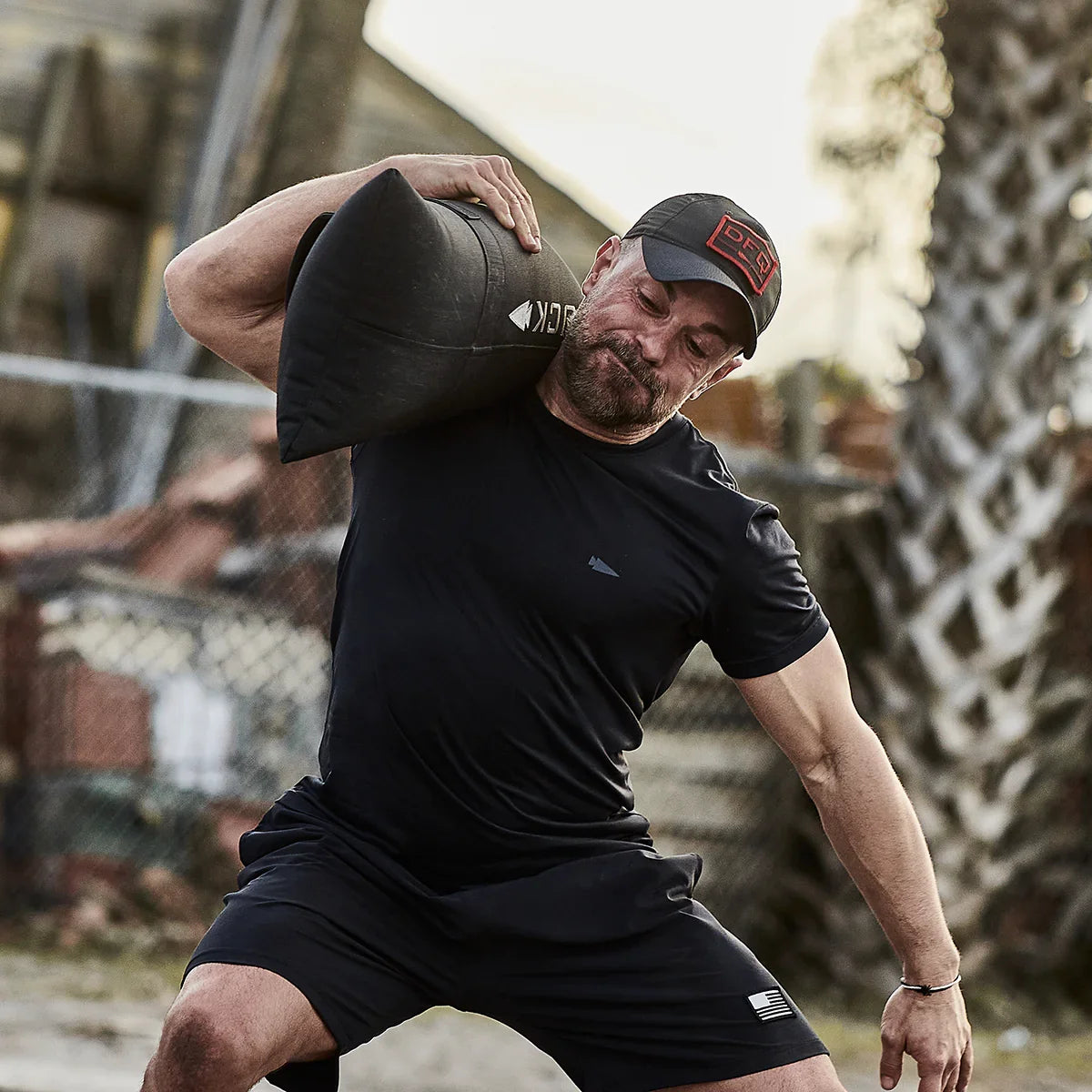 Man lifting GORUCK sandbag outdoors, wearing GORUCK gear, showcasing rucking strength training.