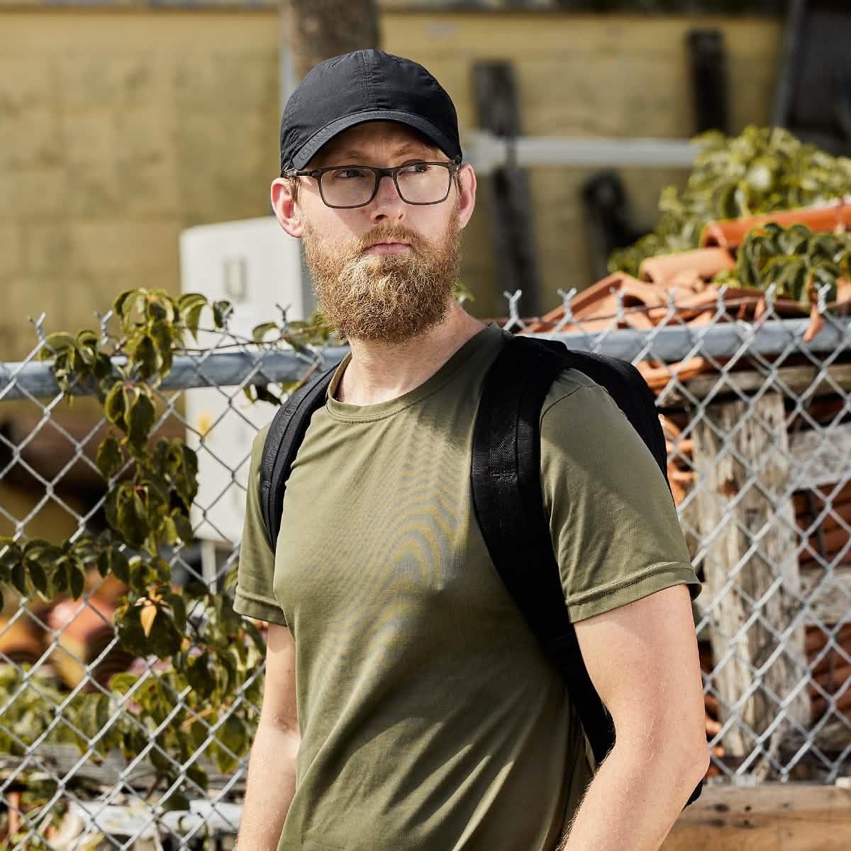 Man wearing black GORUCK hat, olive green shirt, and black backpack outdoors