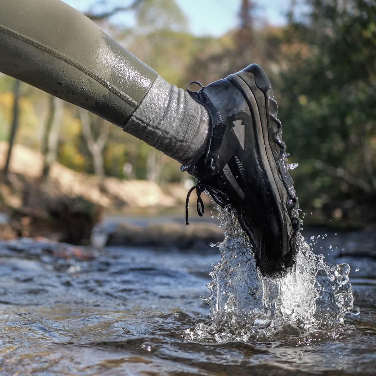GORUCK waterproof black rucking shoe splashing through stream with gray socks and green pants outdoors
