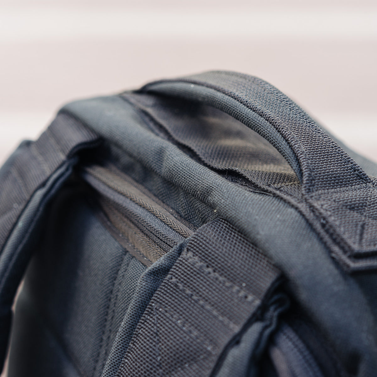 Close-up of a black backpack handle and straps, showing stitching details and fabric texture.