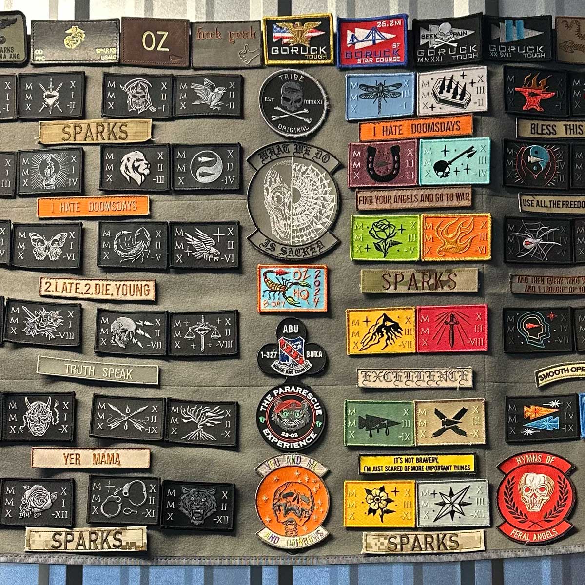 A collection of colorful embroidered patches and name tags displayed on a grey fabric board.