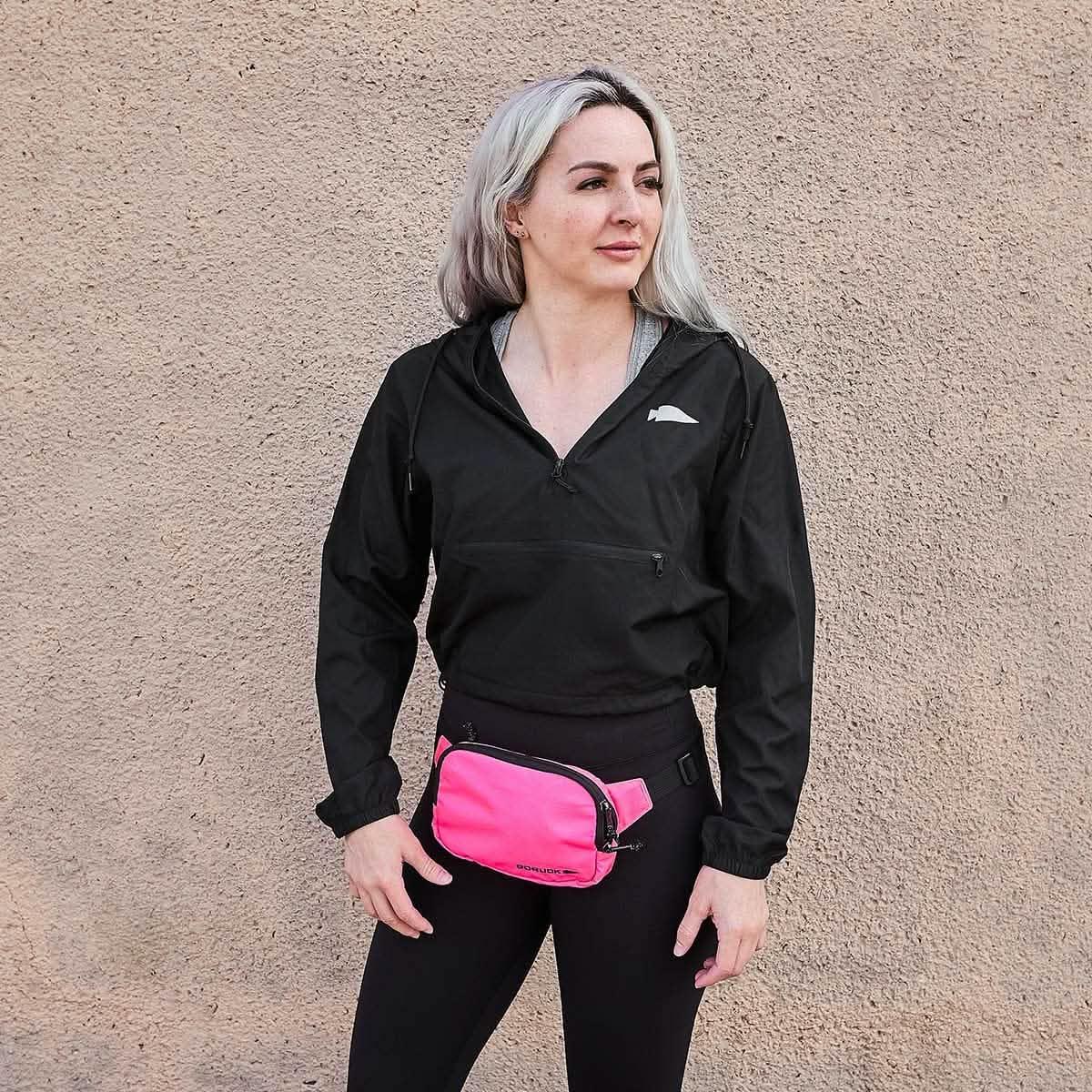 Woman wearing GORUCK waist bag large hot pink against tan textured wall