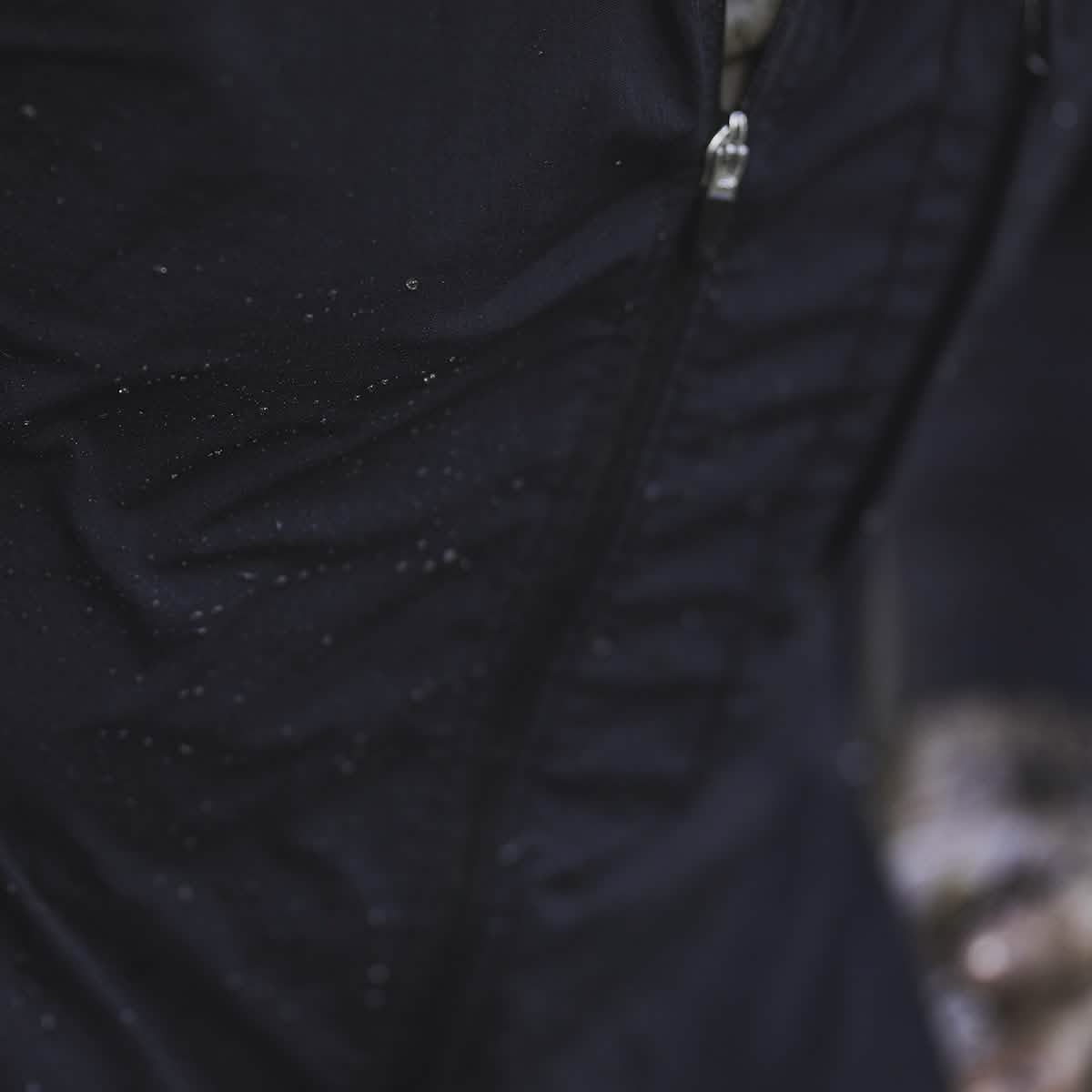 Close-up of a black Indestructible Challenge Windbreaker with a zipper, lightly speckled with water droplets, crafted from abrasion-resistant ToughDry fabric.
