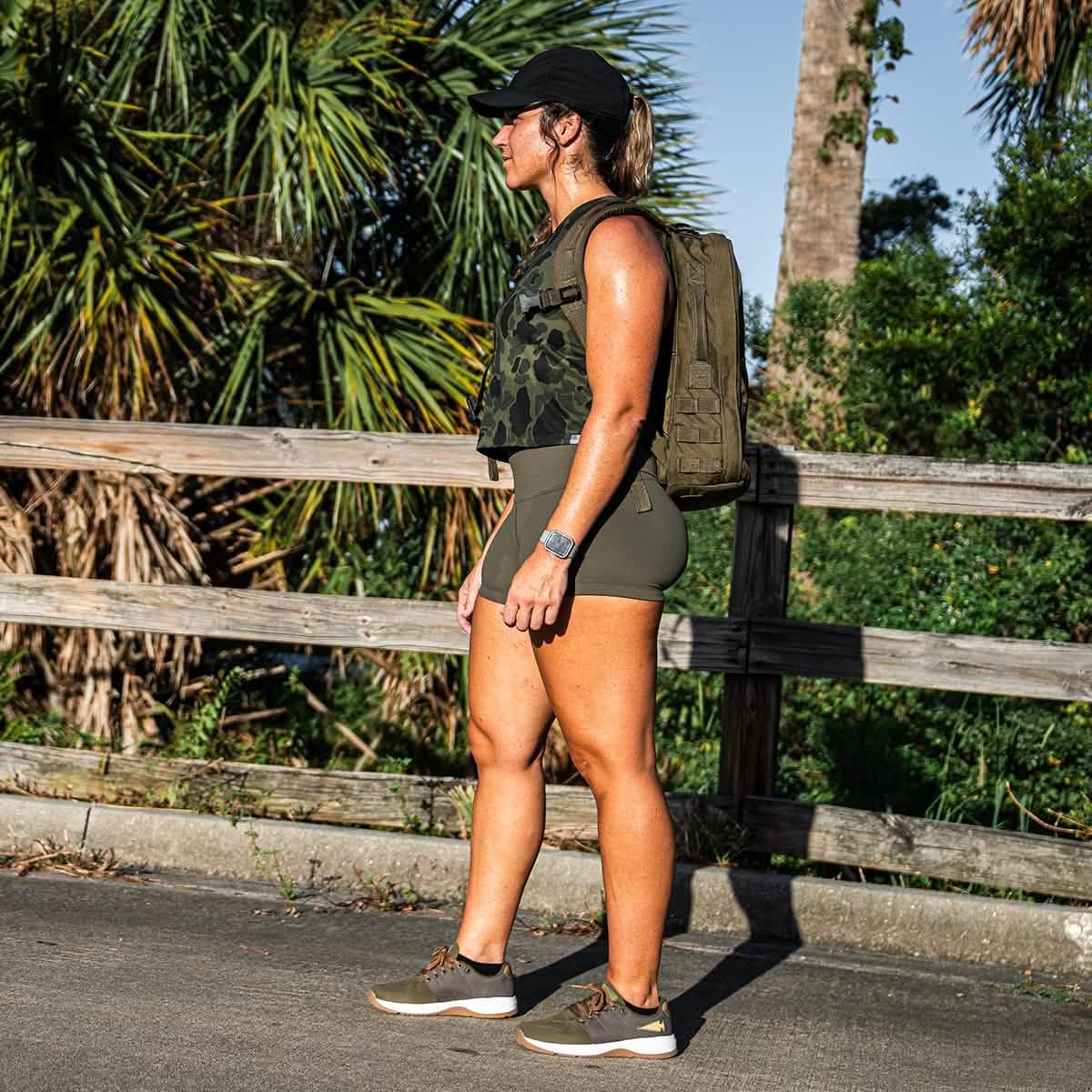 Woman rucking outdoors with GORUCK backpack, wearing athletic gear, palm trees in background