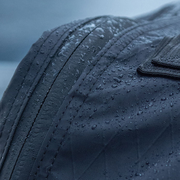 Close-up of a dark fabric bag with water droplets on its surface, highlighting its water-resistant material.