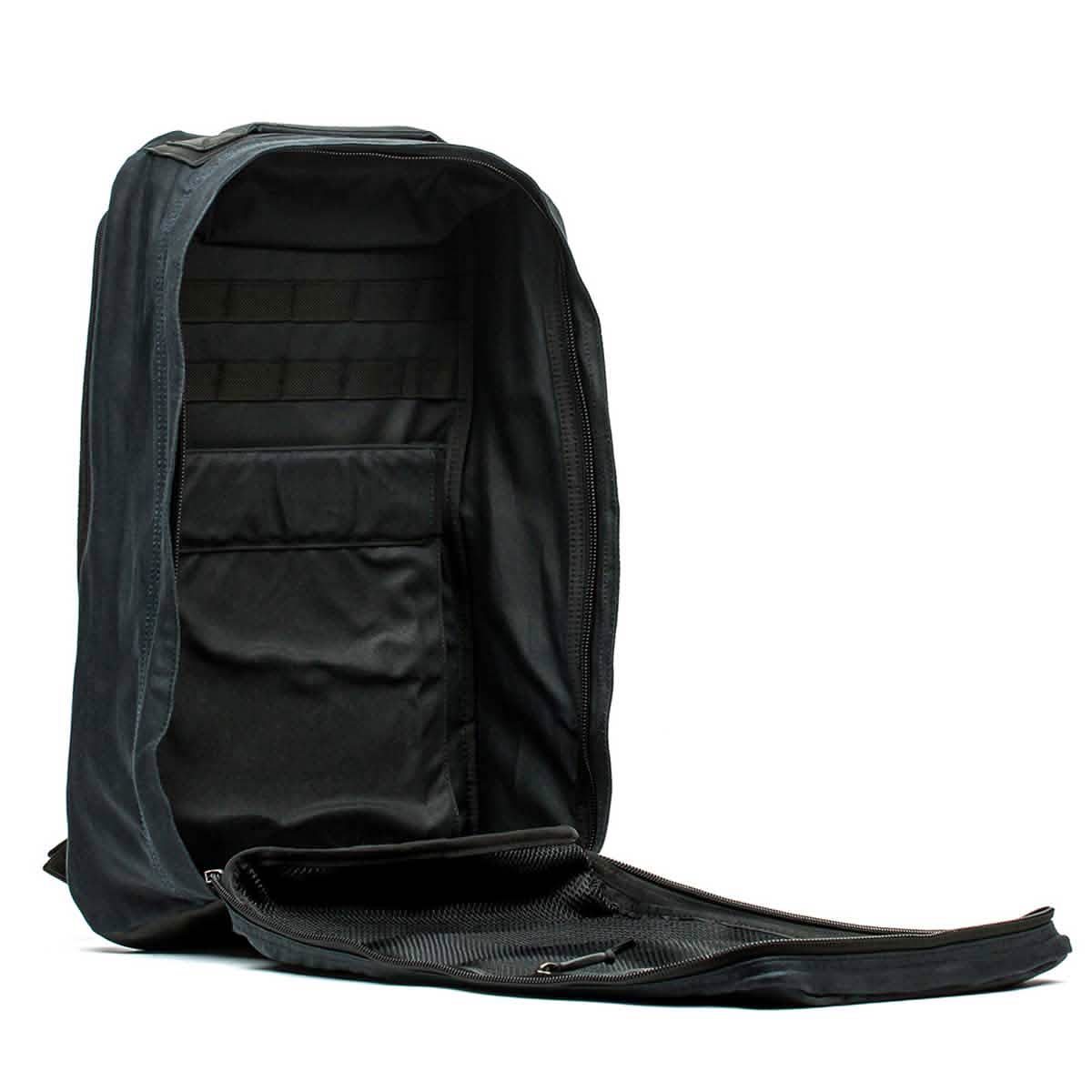 The GR1 USA - Heritage by GORUCK is a black rucksack made from waxed duck canvas with a fully opening main compartment secured by a zipper. Inside, it features multiple organizing sleeves and mesh pockets for efficient storage and easy access, all enhanced by a robust Martexin Wax finish.