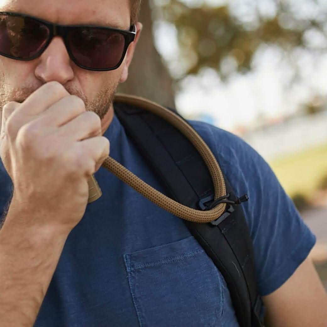 Man wearing sunglasses uses hydration tube with GORUCK rucking backpack outdoors