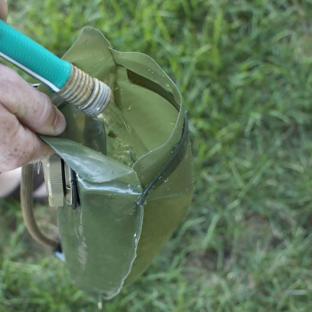 Hand filling olive green GORUCK water bladder with green garden hose outdoors on grass