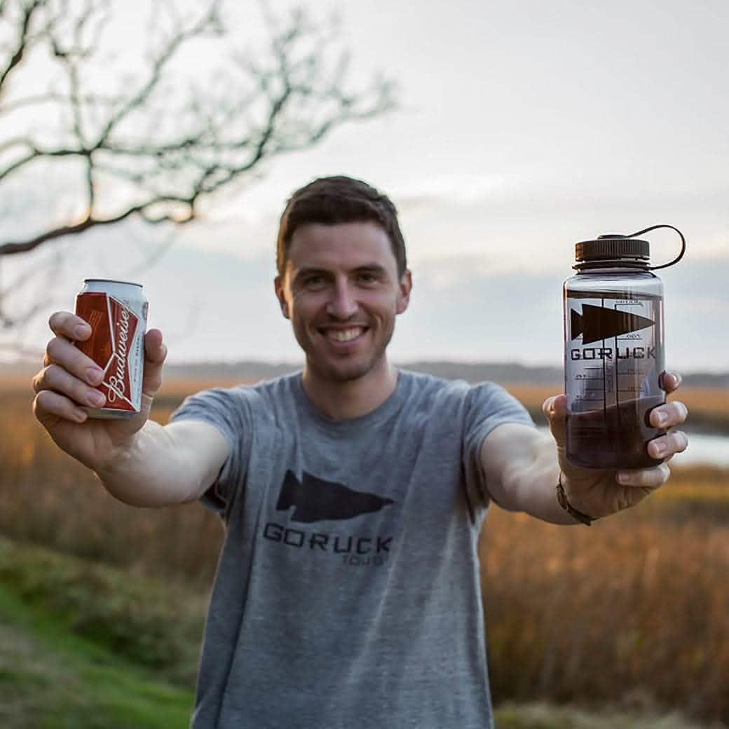 Man outdoors wearing GORUCK t-shirt holding GORUCK water bottle and Budweiser can