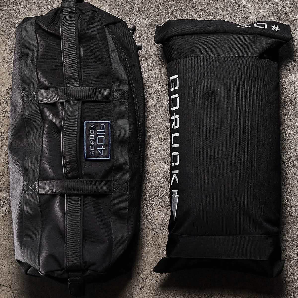 Two black GORUCK Sandbags 2.0 are placed on a textured gray surface. The cylindrical sandbag to the left, crafted from 1000D CORDURA, includes handles and a patch label. Meanwhile, the rectangular sandbag on the right displays the GORUCK logo alongside a white symbol. Both exemplify rugged durability and come with the Scars Lifetime Guarantee.