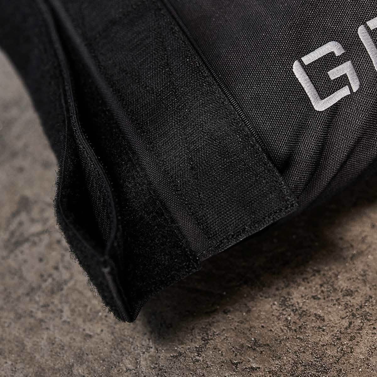 Close-up of a black 1000D CORDURA fabric strap with Velcro on a textured gray surface. The partially visible word GORUCK is printed in white on the fabric, suggesting a label or brand associated with their Sandbags 2.0 product. This image highlights the durable material and precise fastening detail.