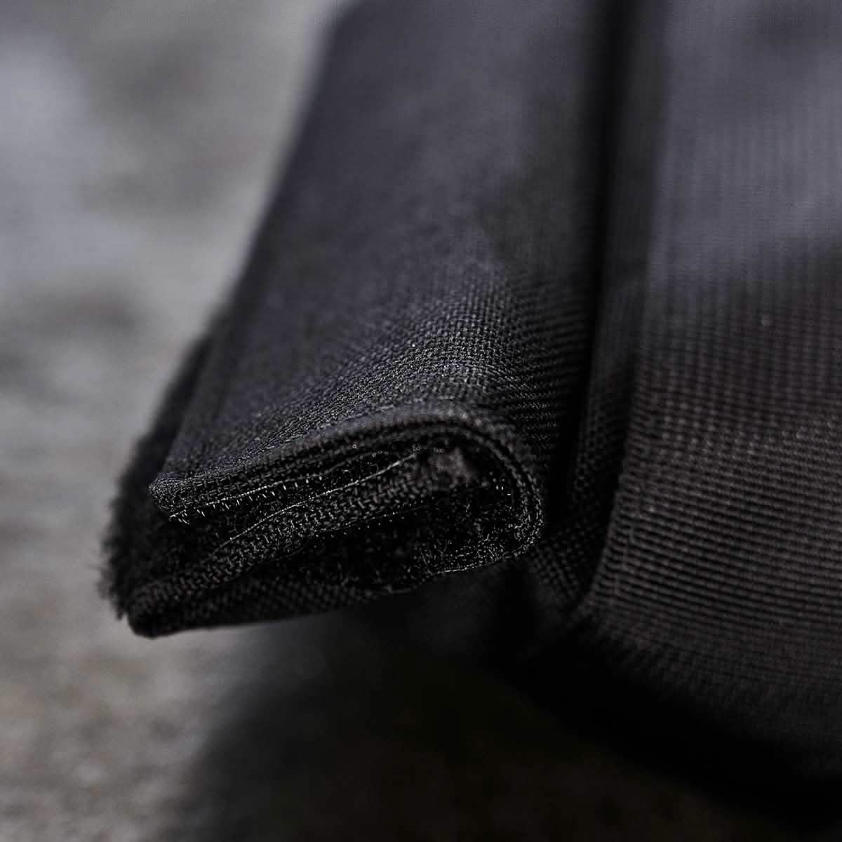 Close-up of a folded corner showcasing the textured black fabric made from durable 1000D CORDURA. The fine weave reveals intricate stitching details against a gray background, embodying resilience similar to GORUCK's Sandbags 2.0.
