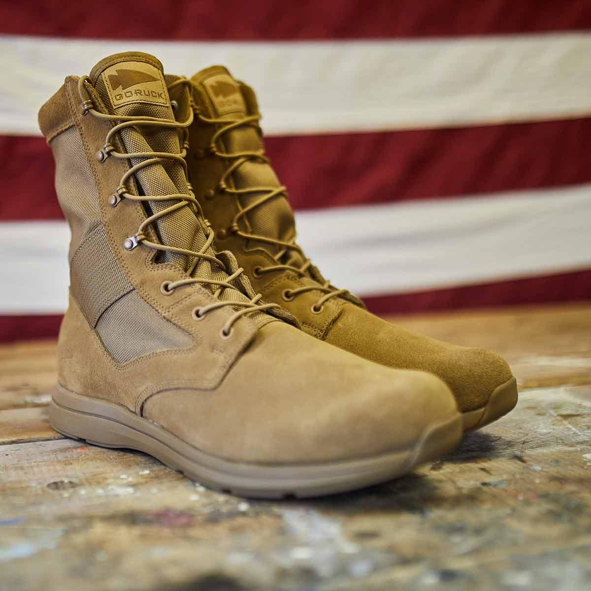 Pair of tan tactical GORUCK rucking boots on rustic wooden floor with American flag backdrop