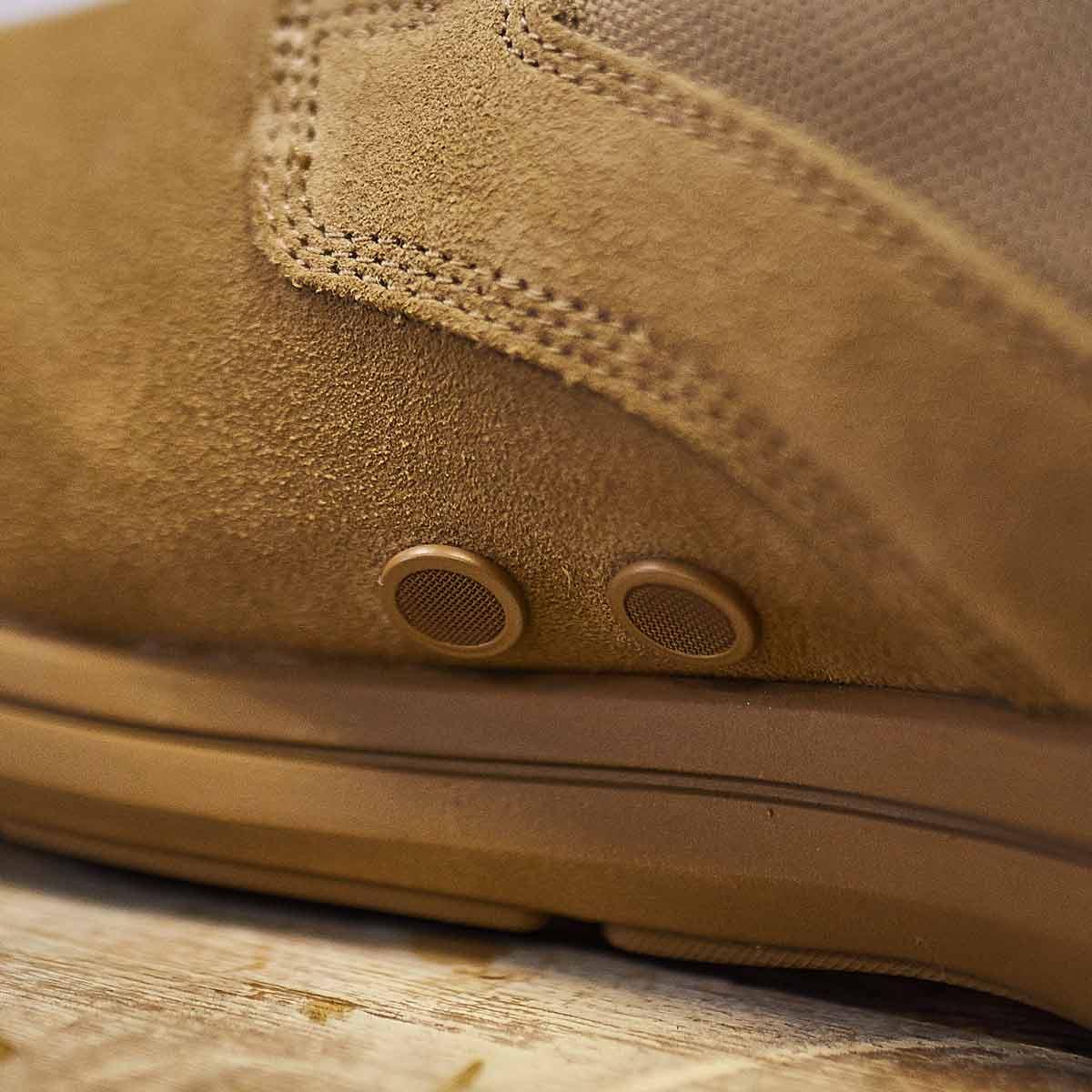 Close-up of coyote-colored suede tactical boot with drainage vents and detailed stitching on wooden surface