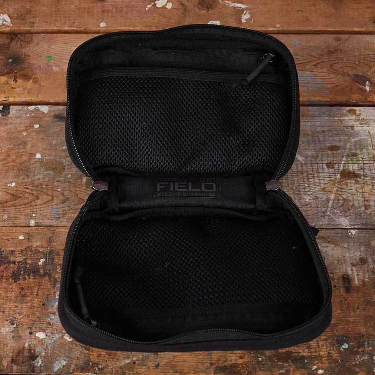 Open black GORUCK Field Pocket with dual mesh zipper compartments on worn wooden surface