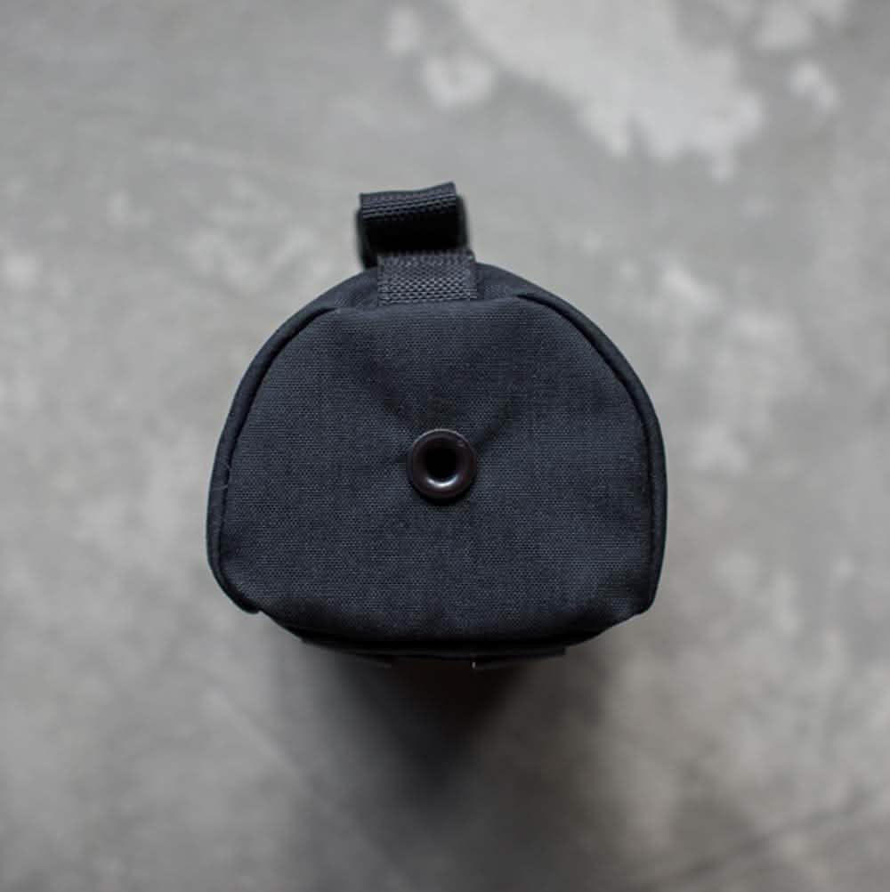 A top-down view of a black cylindrical pouch with a strap on a gray textured surface. The GORUCK Full Panel Water Bottle Pocket features a central circular opening, perfect for securely holding your water bottle while on the move.