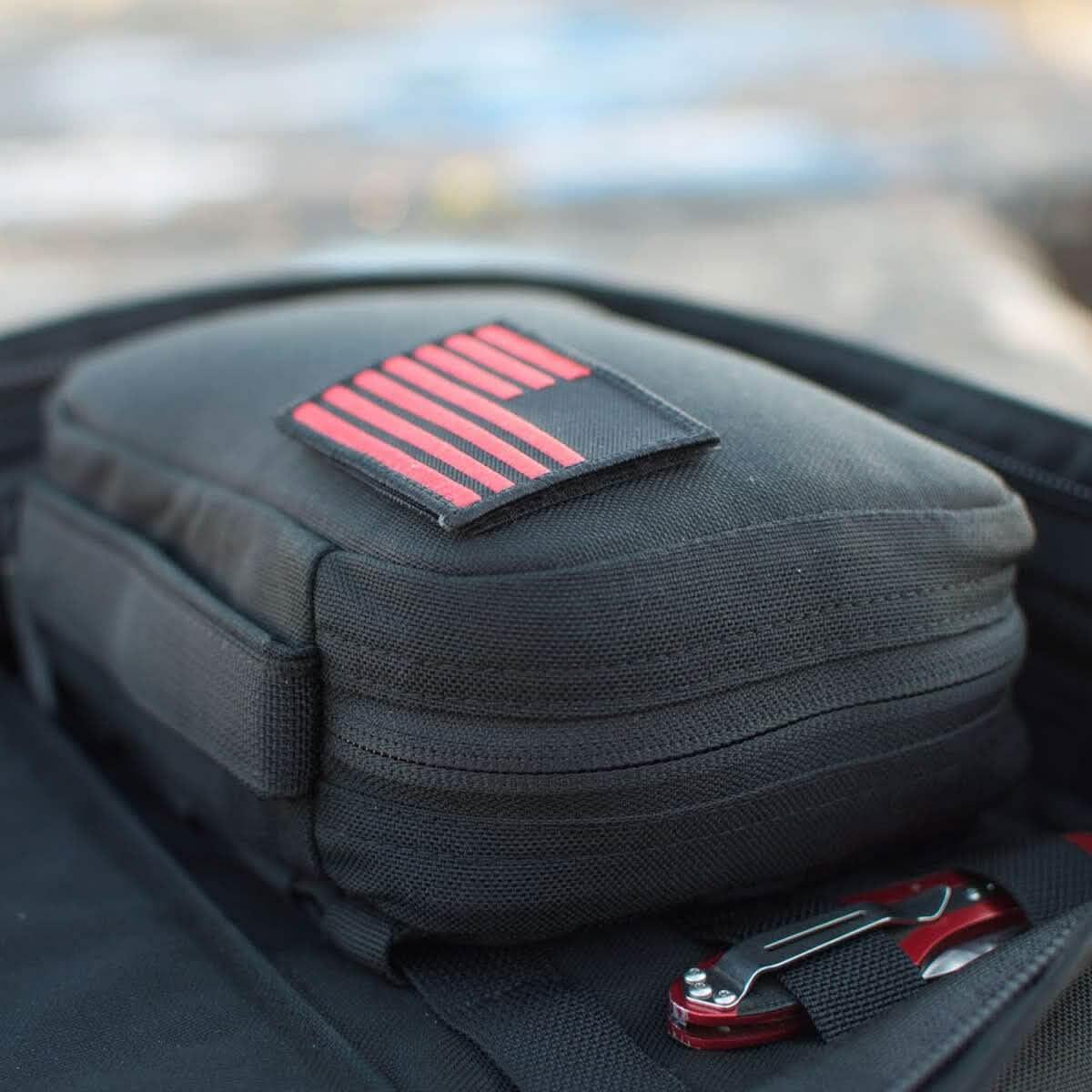 Black GORUCK MOLLE pouch with red flag patch inside a larger black bag, featuring a red multi-tool