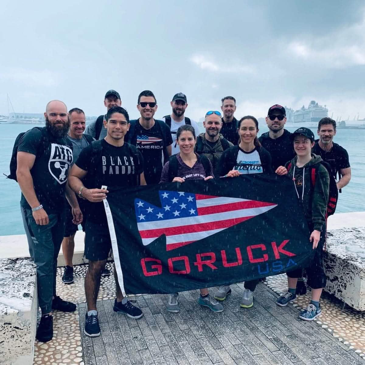 Group of people holding GORUCK USA flag outdoors by waterfront in rainy weather