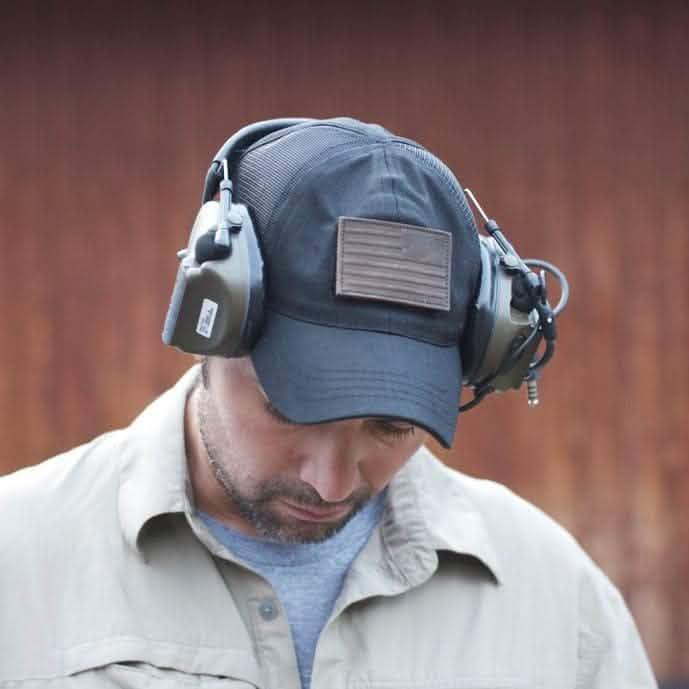 Man wearing black cap with leather reverse flag patch and ear protection, GORUCK tactical gear