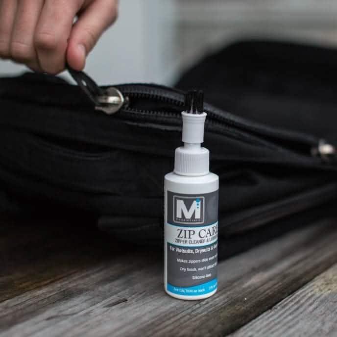Zip Care zipper cleaner bottle beside a black GORUCK bag with a hand holding the zipper