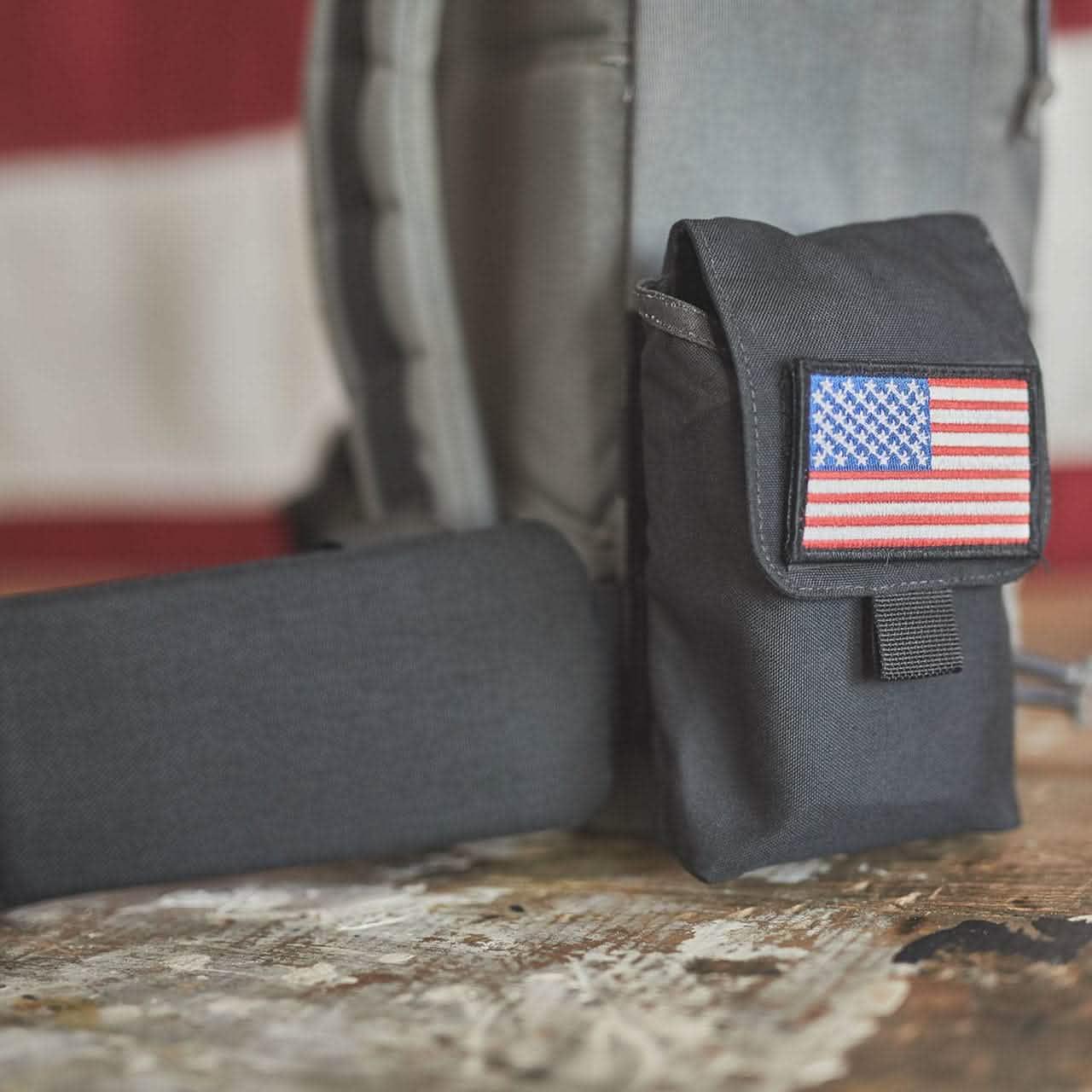 Black tactical pouch with American flag patch on a worn wooden surface, part of rugged GORUCK gear