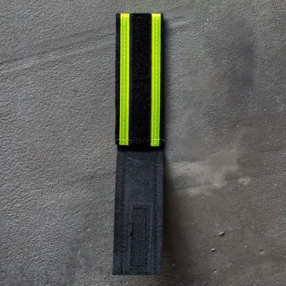 The Reflective Ruck Bands from GORUCK include a black fabric strap with two bright yellow reflective stripes on a gray surface to enhance nighttime visibility and feature a Velcro fastener for secure attachment.