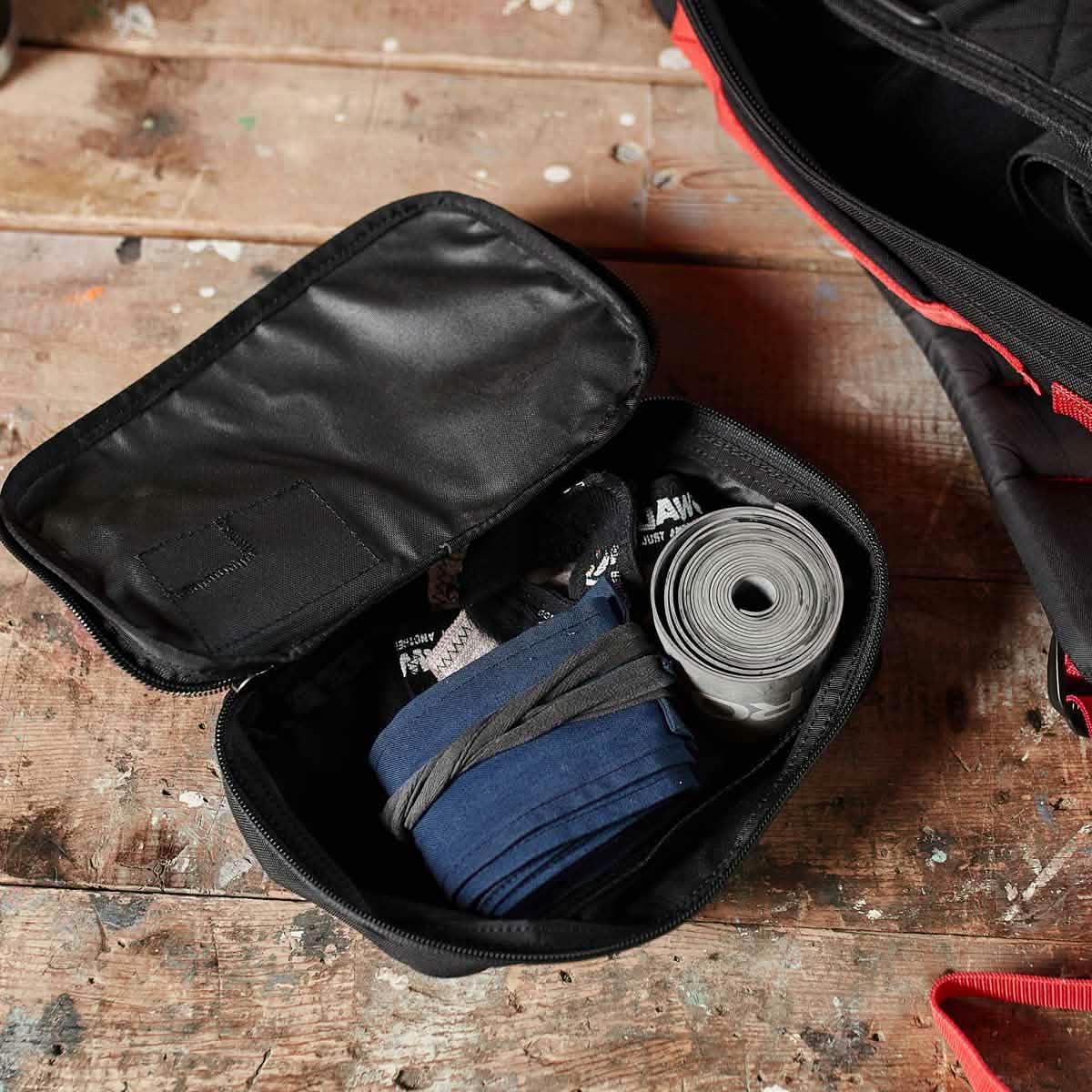 Black GORUCK Shadow Pocket M packed with rucking tape and elastic bands on wooden floor