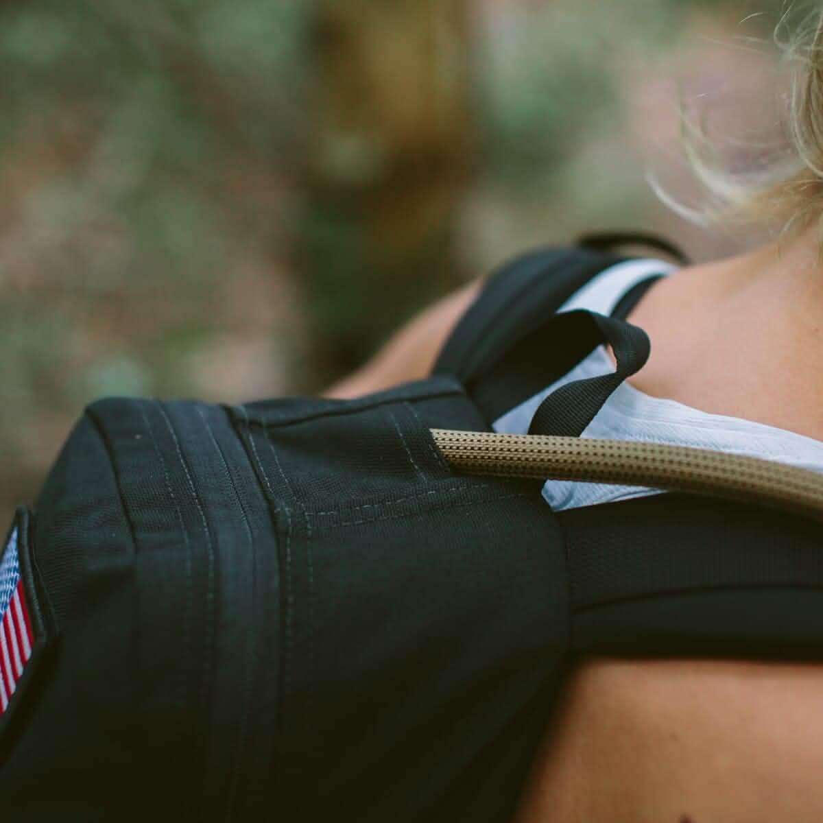 Close-up of black GORUCK backpack with hydration tube, worn by person outdoors
