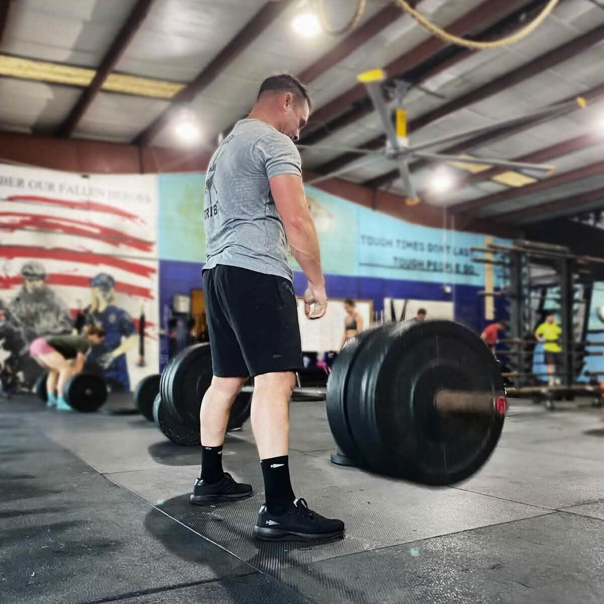 Man lifting heavy barbell in gym with patriotic wall mural and fitness equipment in background